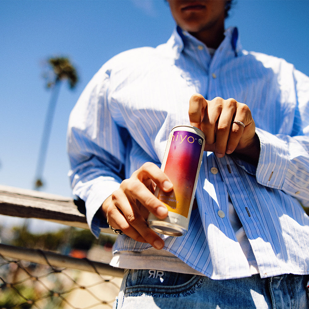 Person holding a colorful can of non-alcoholic functional seltzer hiyo with a blurred outdoor background