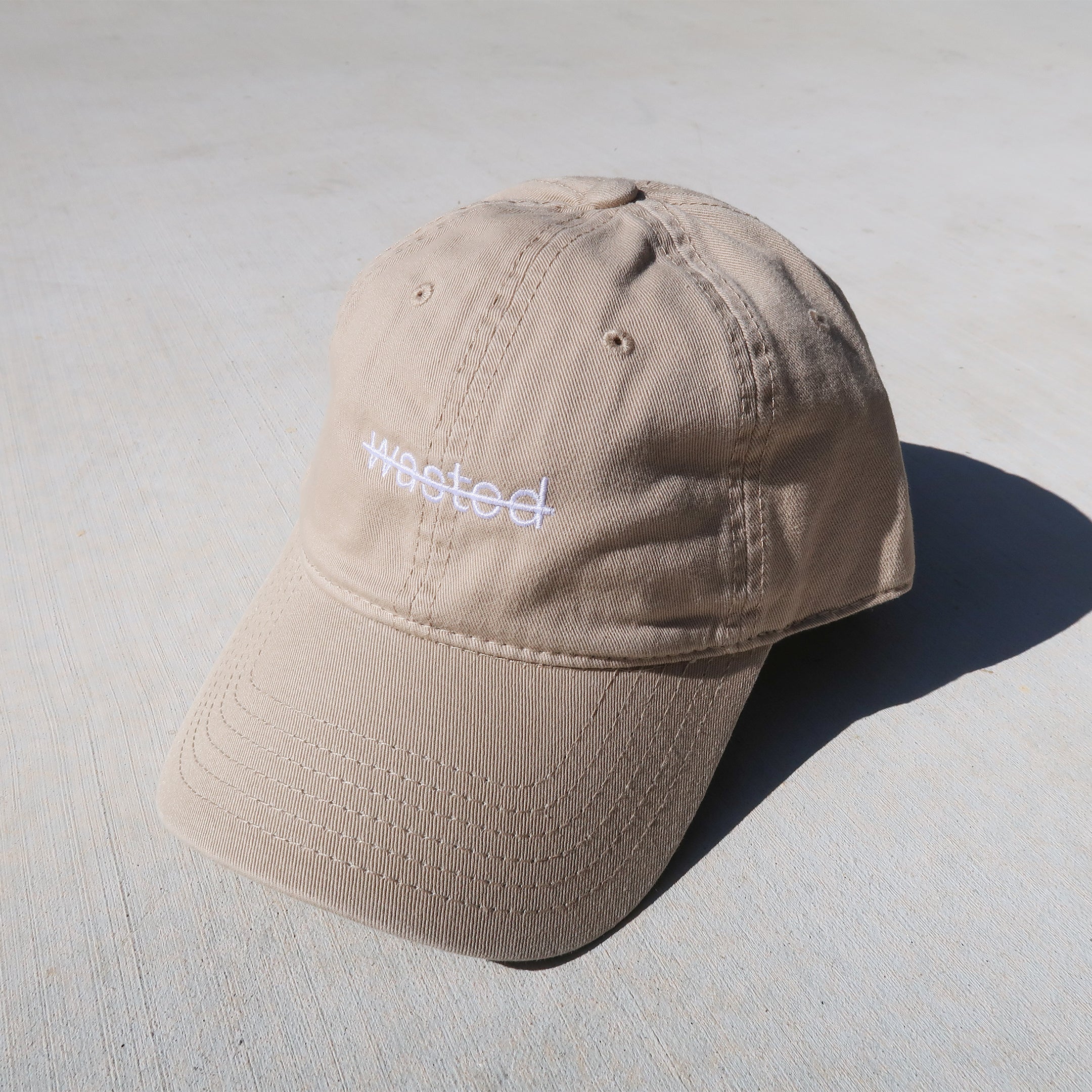 a khaki dad cap. cap includes the text 'wasted' struck through and embroidered across the front center in white.