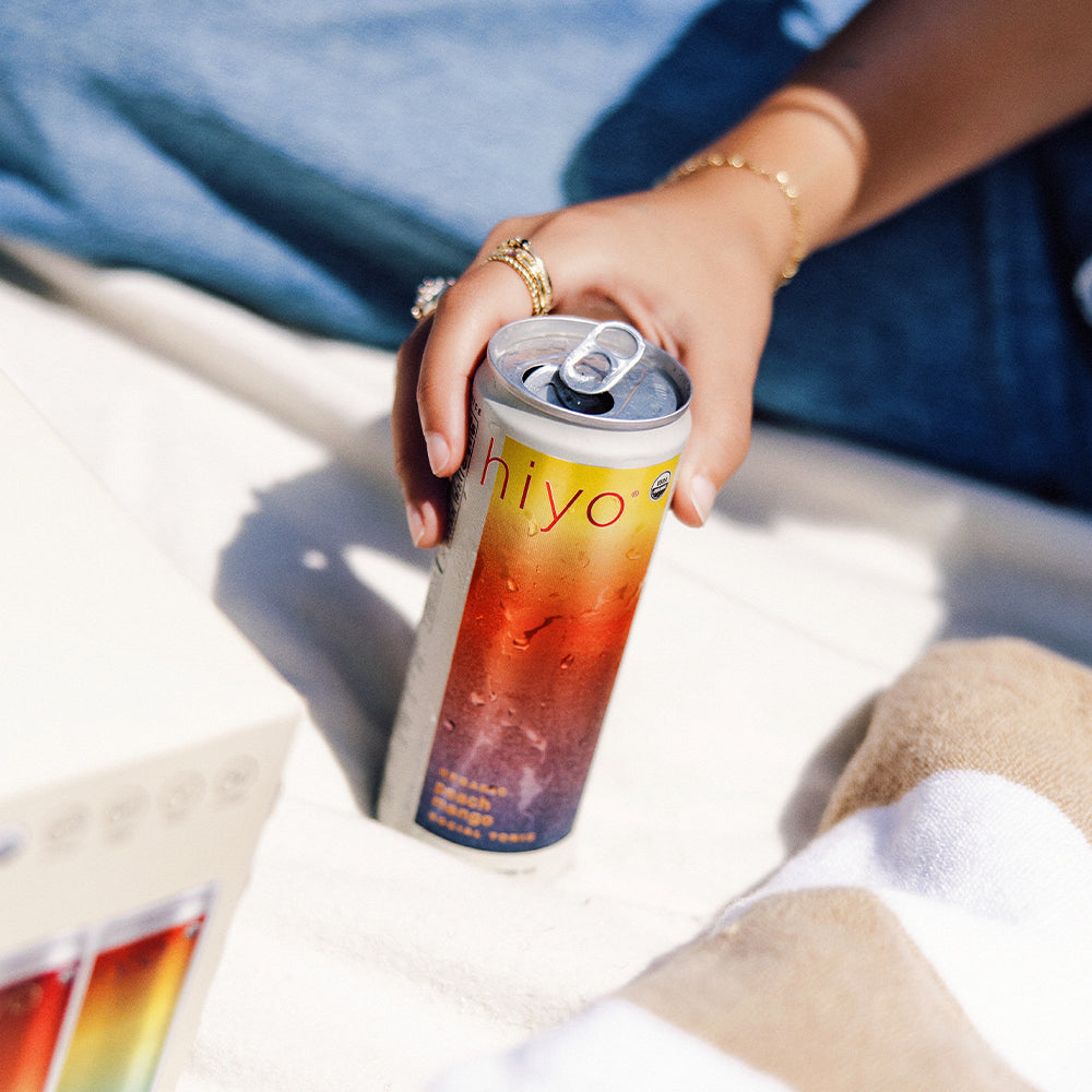 Person holding a colorful can with non-alcoholic functional seltzer hiyo on a sandy surface