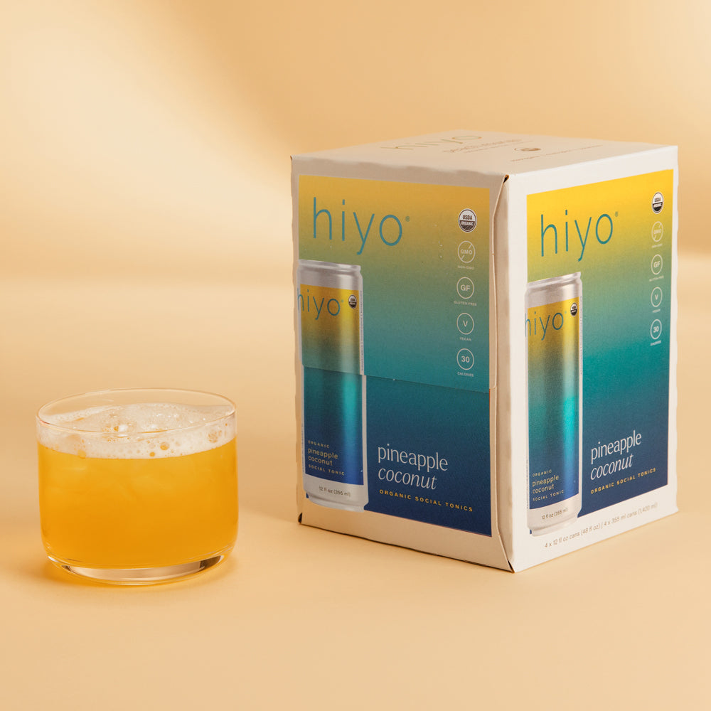 non-alcoholic hiyo pineapple coconut drink with a glass of the drink on a beige background