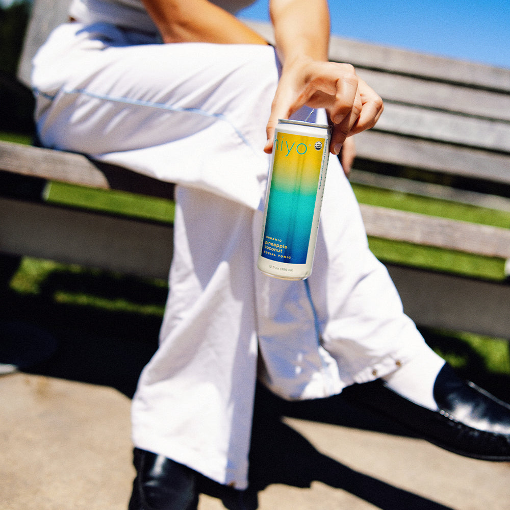 Person holding a can of non-alcoholic functional seltzer hiyo water on a bench with a blue sky background