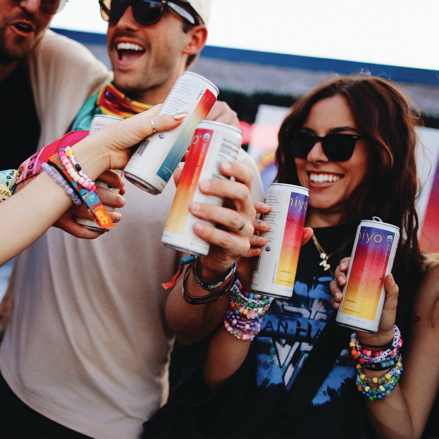 a group of friends smiling and laughing while cheersing cans of hiyo.