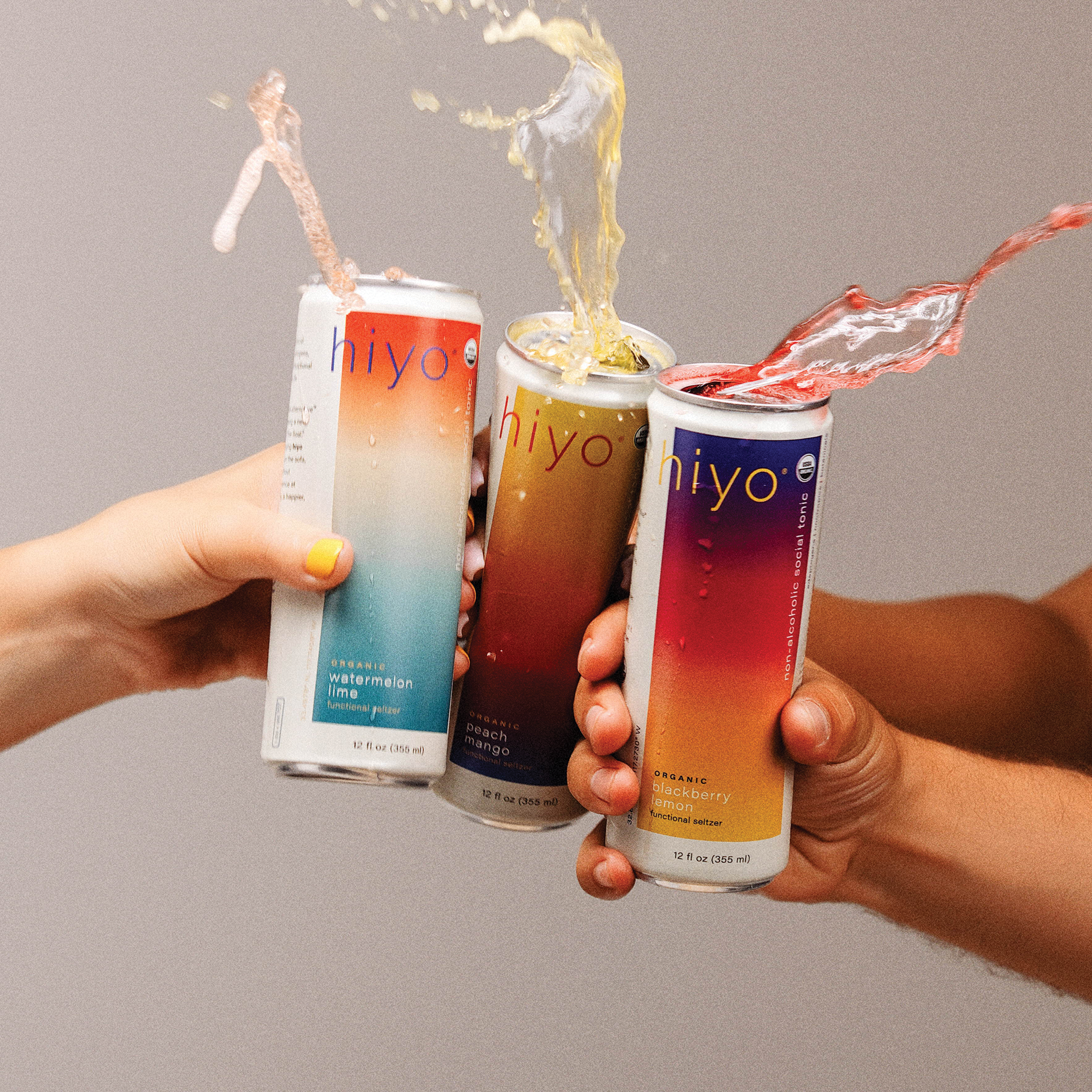 hands toasting the three original flavors of hiyo: watermelon lime, peach mango, and blackberry lemon (from left to right).