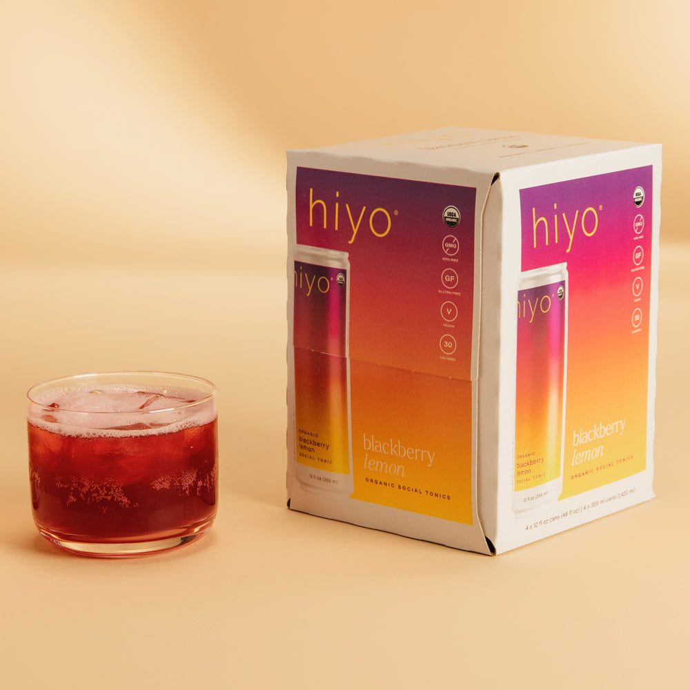 Four-pack of Hiyo blackberry lemon organic social tonics with one bottle served over ice in a glass.