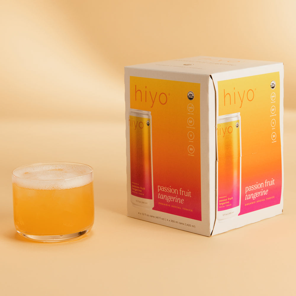 Four-pack of Hiyo passion fruit tangerine sparkling beverage with gradient orange-to-pink packaging and glass of poured drink
