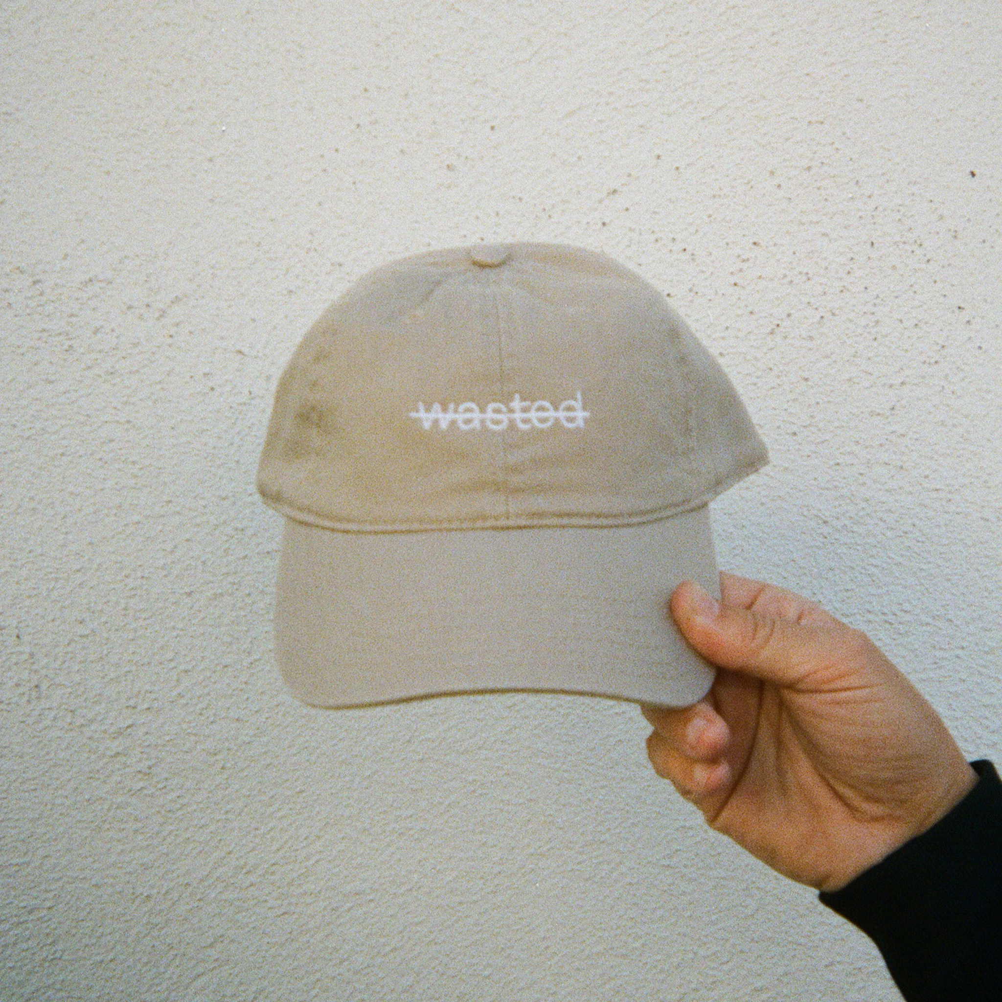 a khaki dad cap. cap includes the text 'wasted' struck through and embroidered across the front center in white thread.