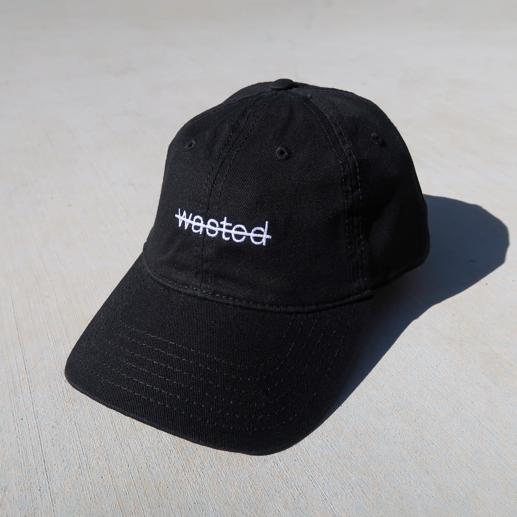 a black dad cap. cap includes the text 'wasted' struck through and embroidered across the front center in white.