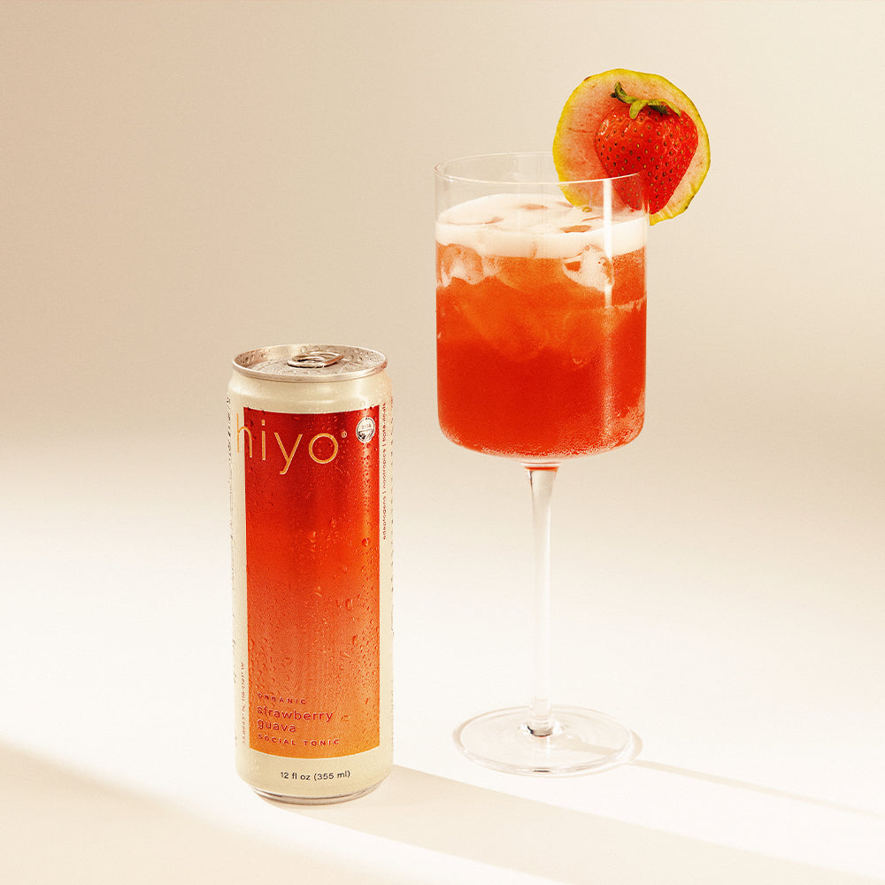 Mocktail in a glass with a strawberry garnish next to a can labeled 'hiyo' on a light background