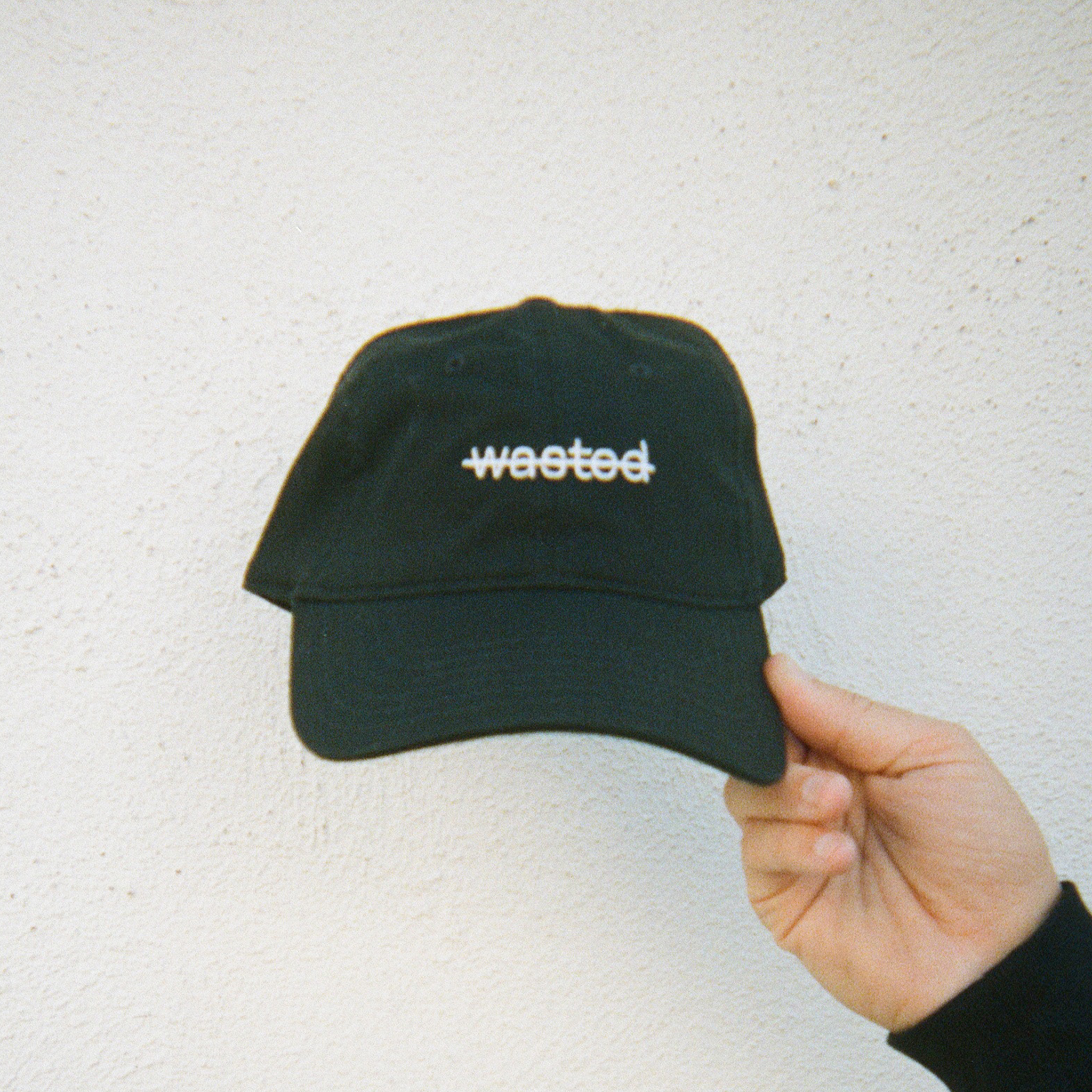 a black dad cap. cap includes the text 'wasted' struck through and embroidered across the front center in white thread.