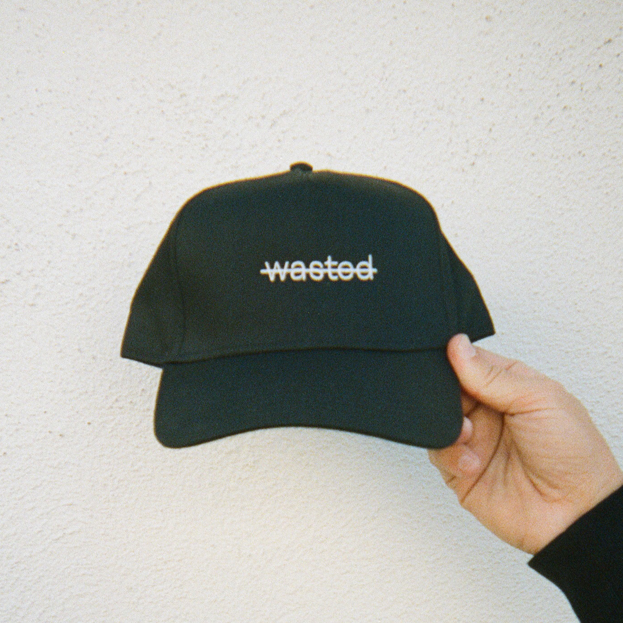 a black trucker hat. hat includes the text 'wasted' struck through and embroidered across the front center in white thread.