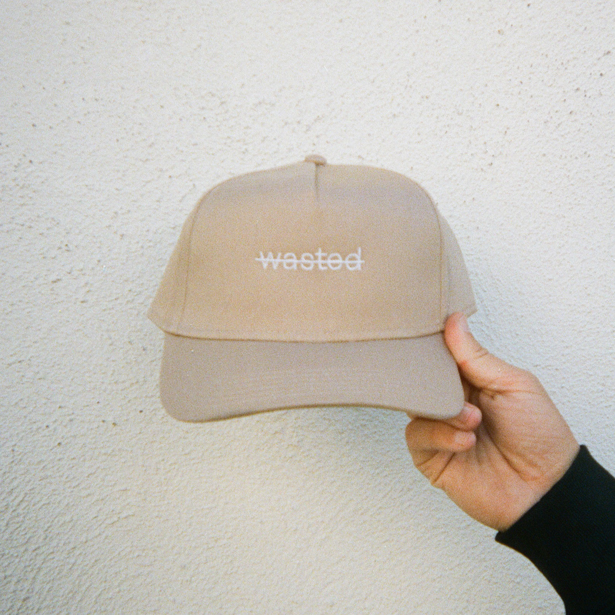 a khaki trucker hat. hat includes the text 'wasted' struck through and embroidered across the front center in white thread.